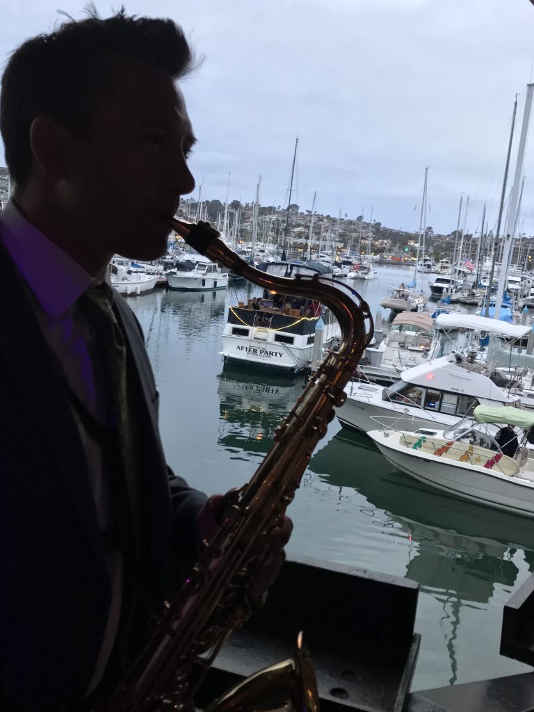 Silhouette of man playing saxophone with boats in background