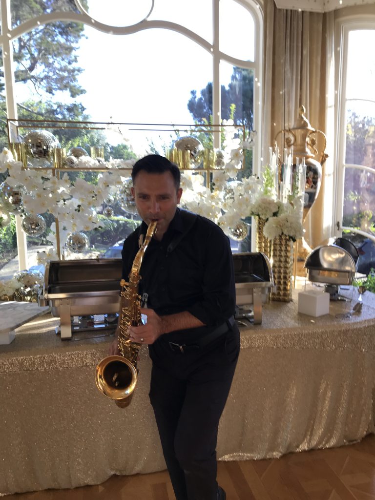 Saxophonist playing music in front of catering display and decorations inside a mansion